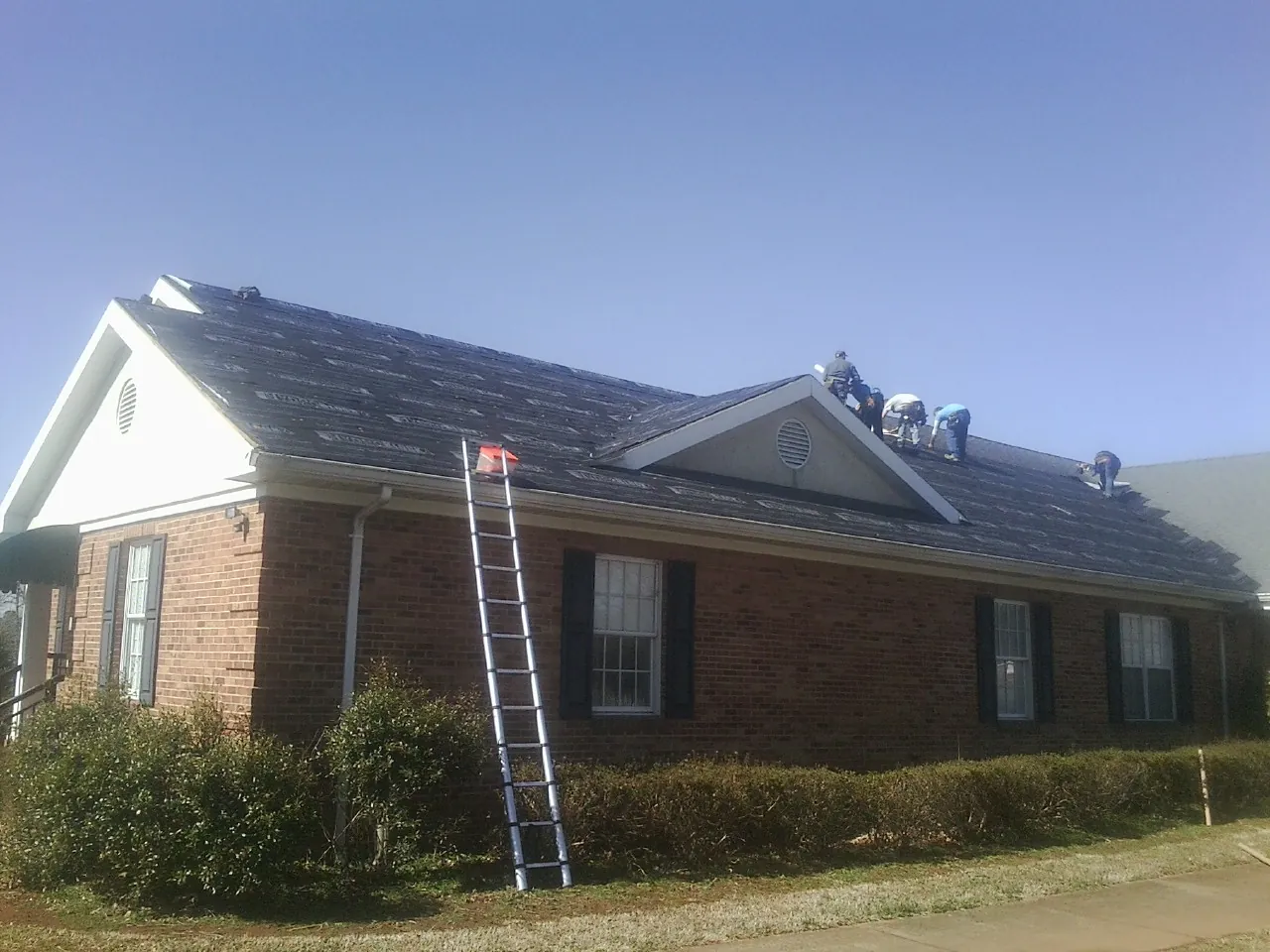 Crew tearing shingles off a brick ranch roof with a ladder set — Metal Roof Repair work by our crew in Gap