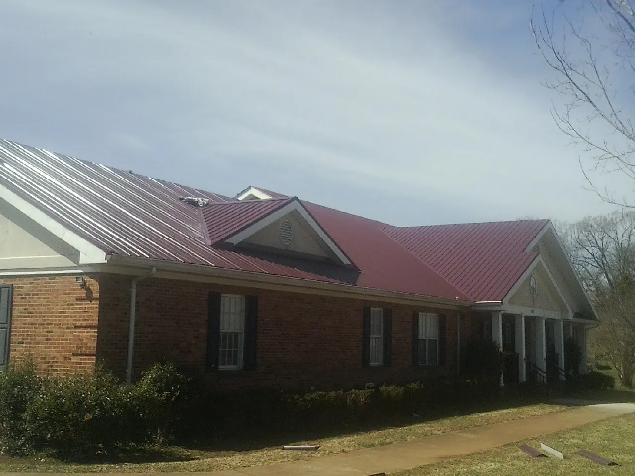 Red metal roof with gabled entries on a long brick building, from a Hail Damage Roof Repair job in Gap