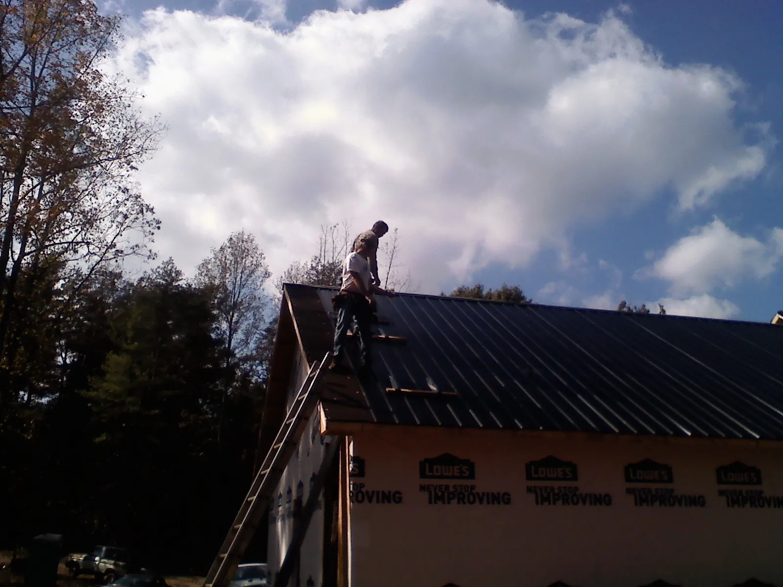 Roofer fastening dark metal panels high against a cloudy sky, from a Roof Inspection job in Gap